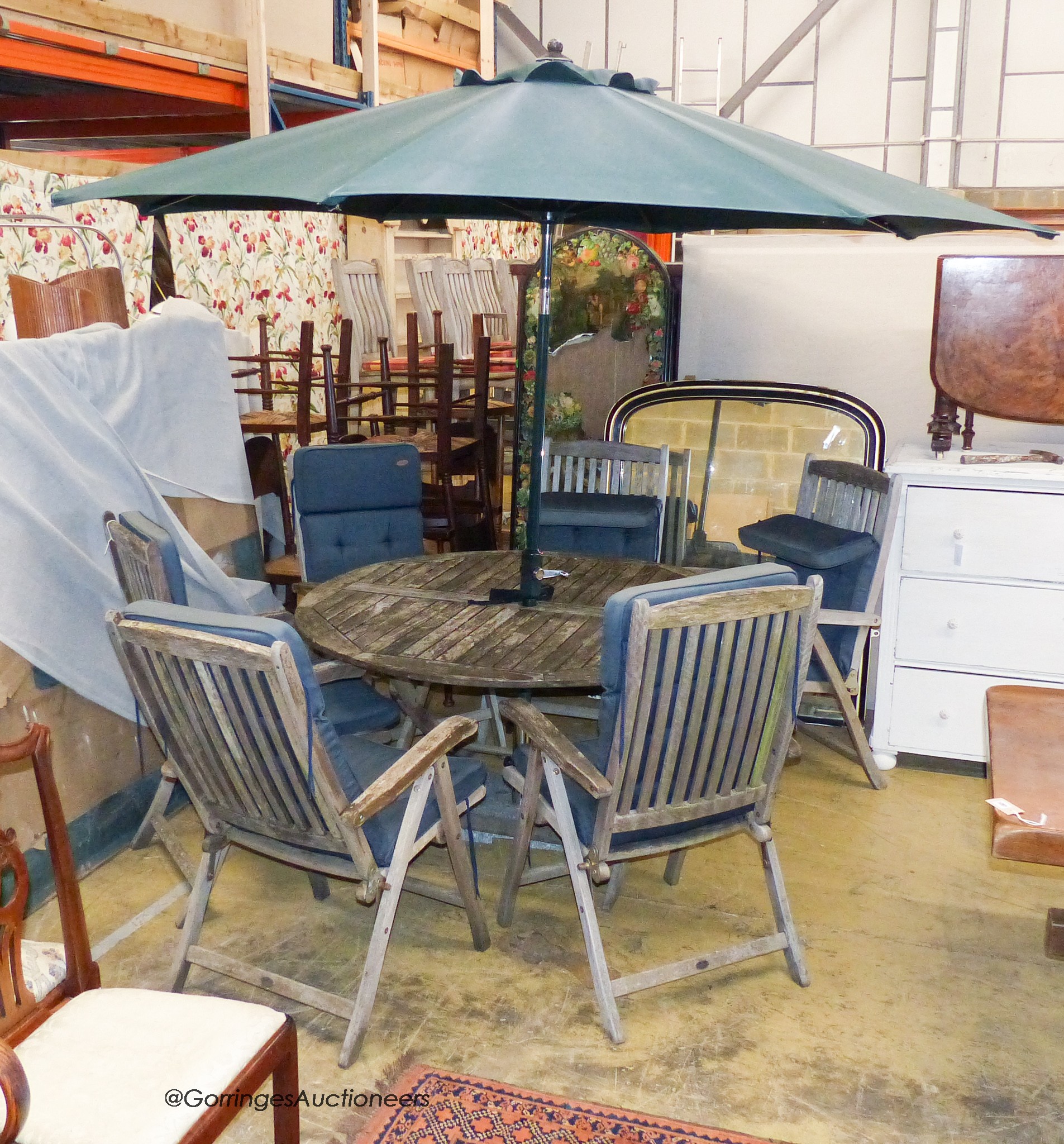 An Alexandra rose weathered teak garden circular table, 140cm diameter six folding elbow chairs with cushions and a canvas crank parasol with cast stone base